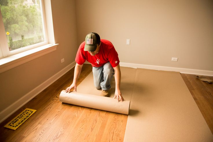Worker unrolling brown floor protection paper over a hardwood floor